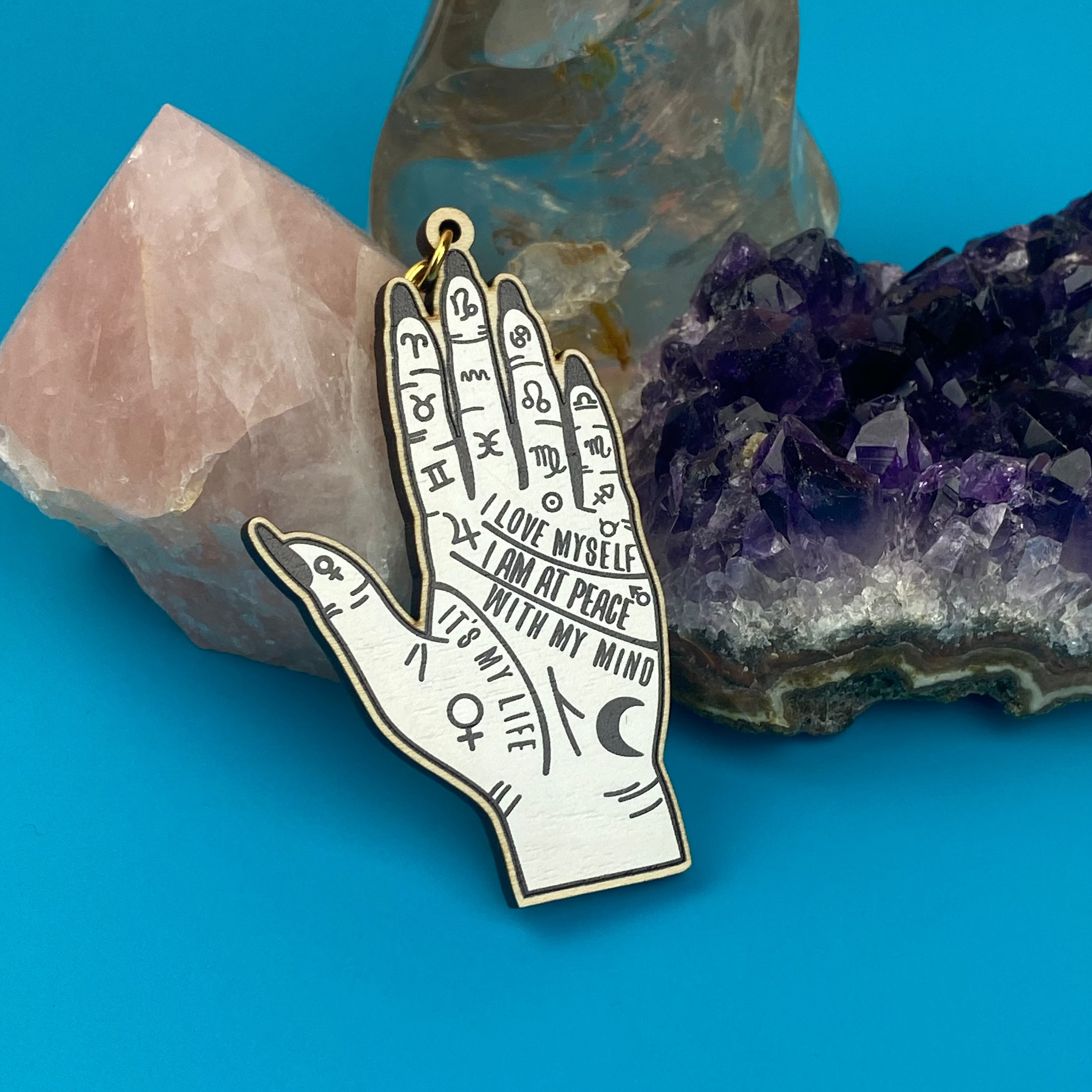 Hand-shaped pendant with inscriptions on a blue background with crystals