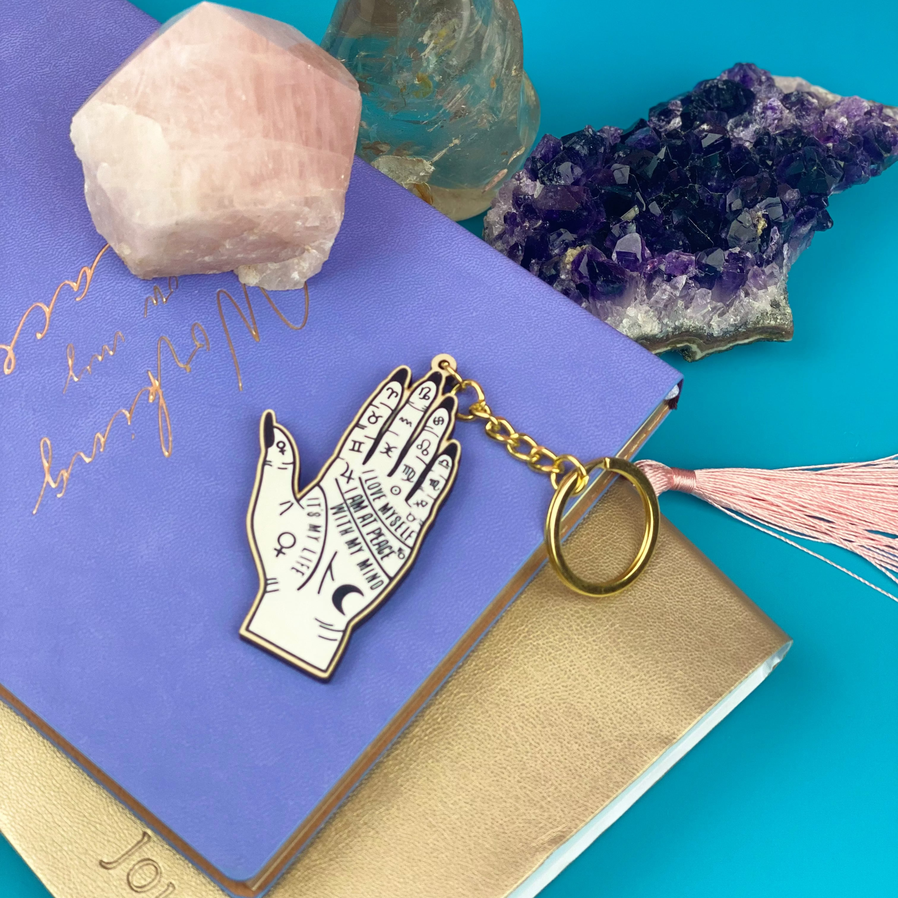 Decorative keychain with palm design on a blue background with crystals and a journal.