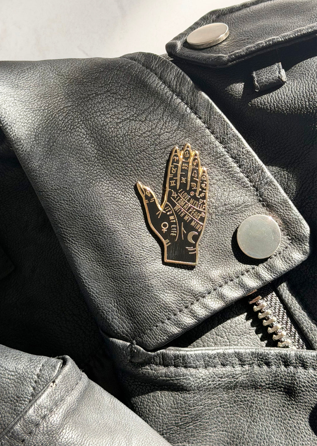 Black leather jacket with a gold embossed hand design on a light gray background