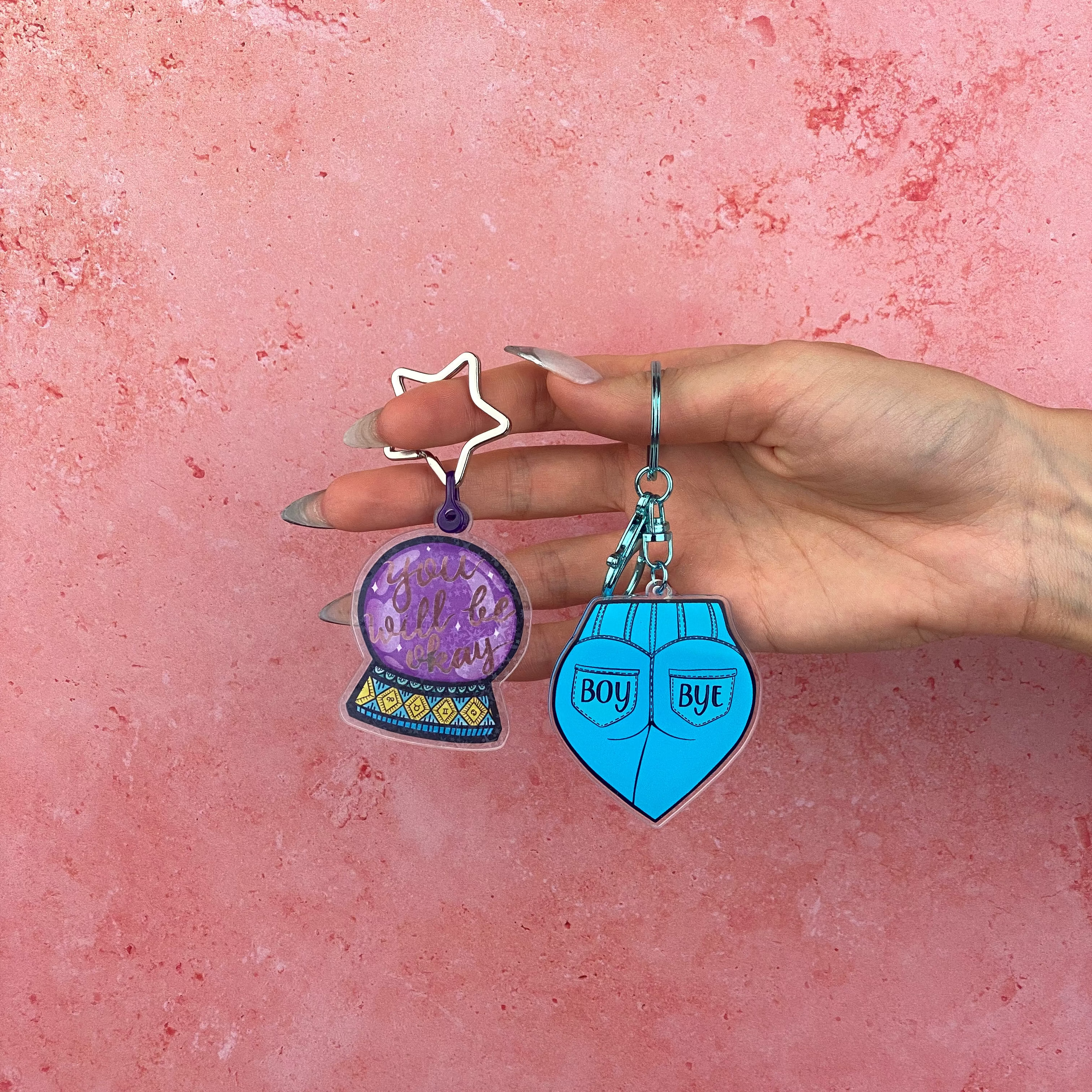 Hand holding two keychains against a pink background