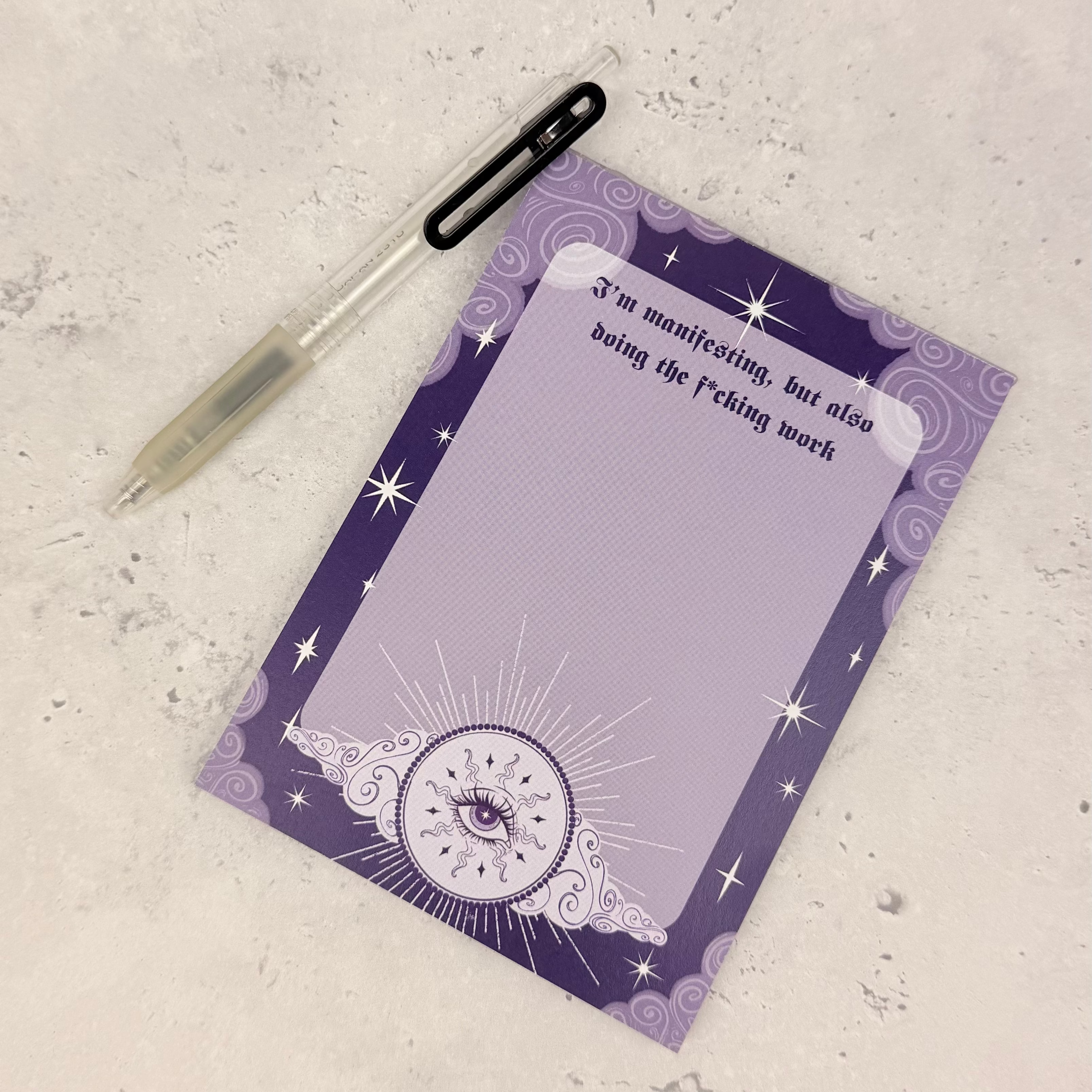 Purple notepad with star and moon design on a textured surface with a pen.