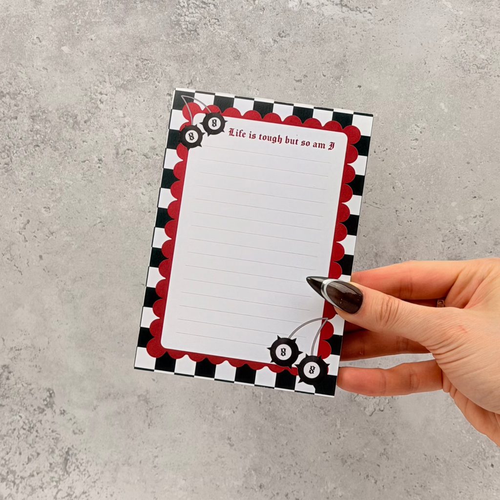 Hand holding a decorative notepad with a red and black border on a gray surface