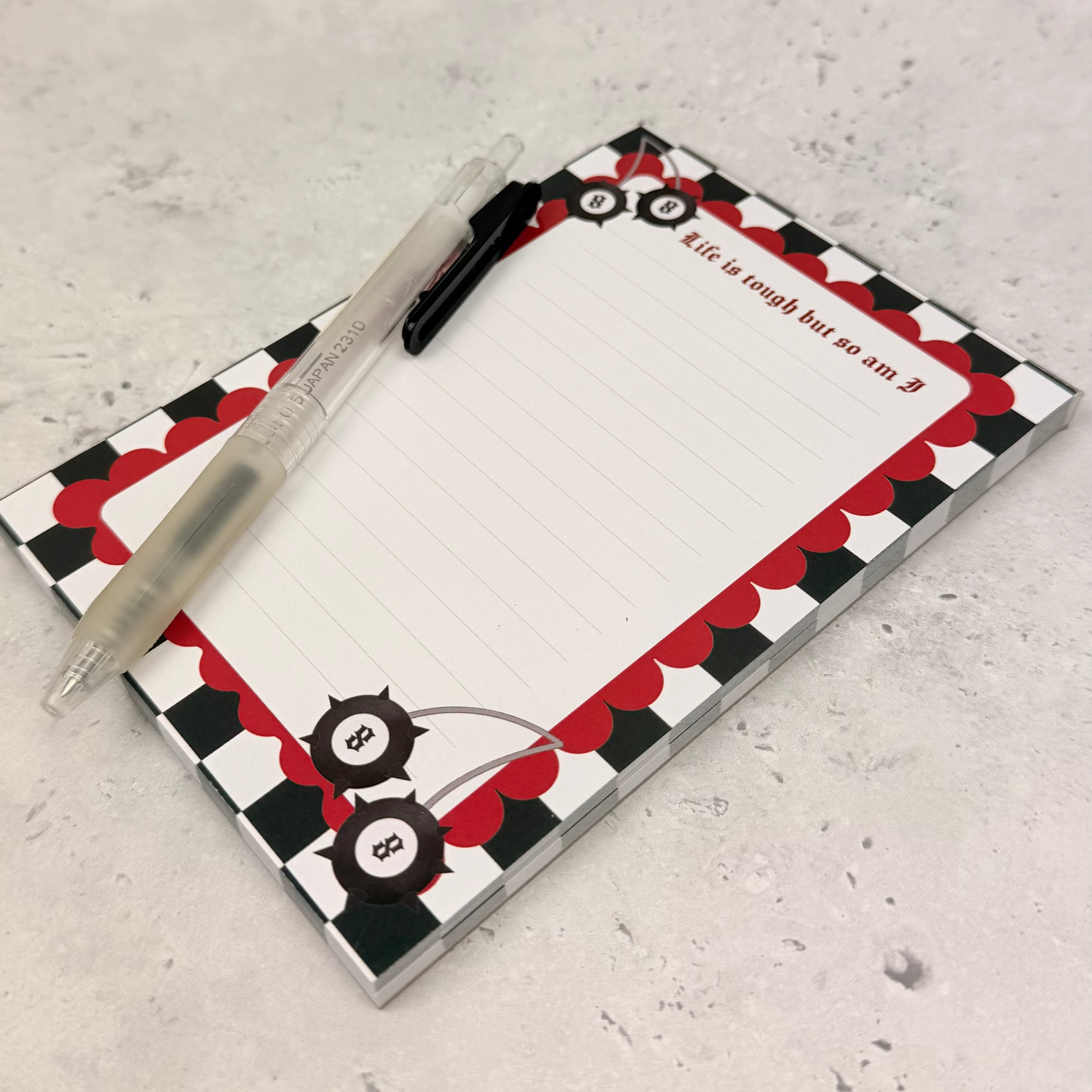 Notepad with a red and black checkered border and a pen on a gray surface