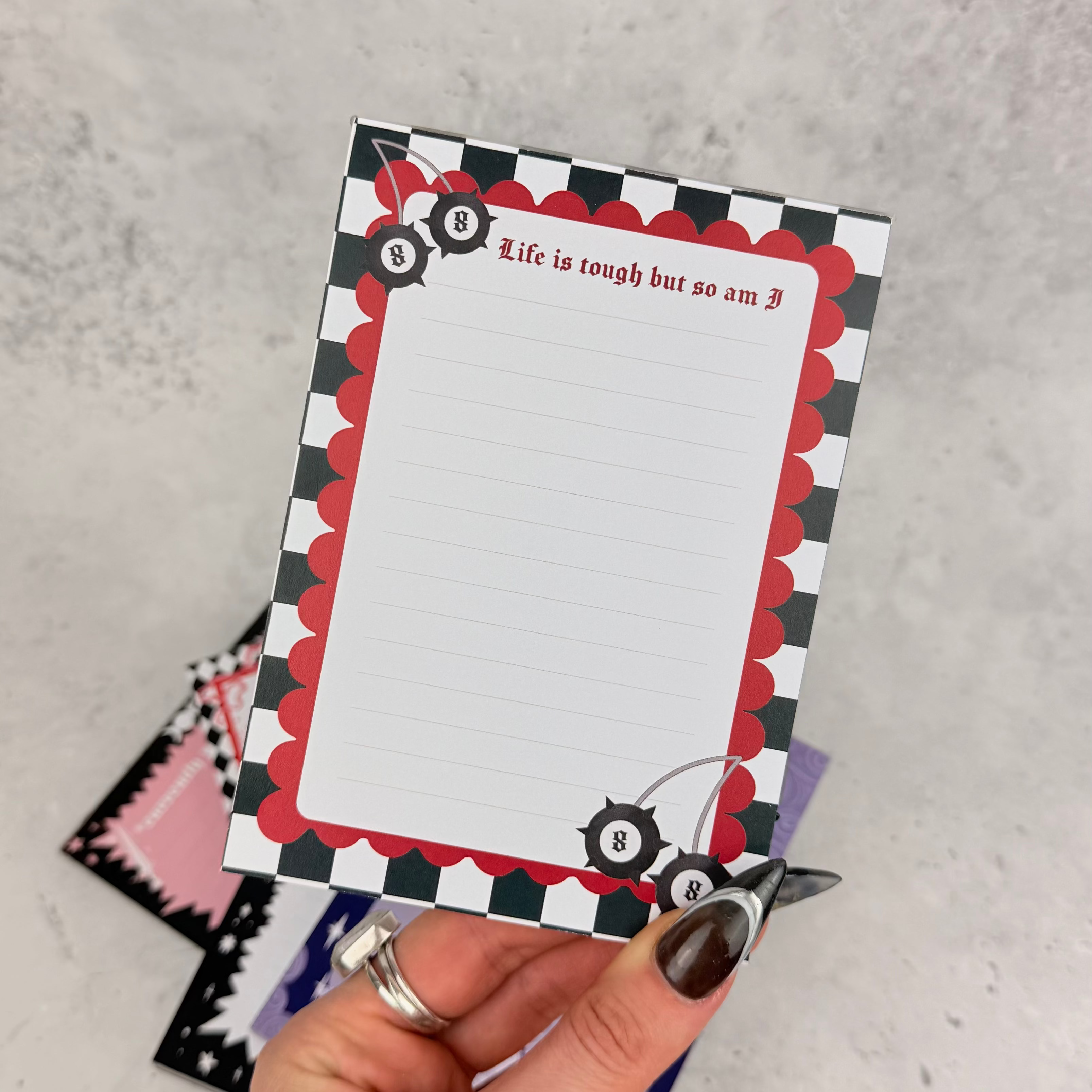 Hand holding a decorative notepad with checkered border and text on a gray surface