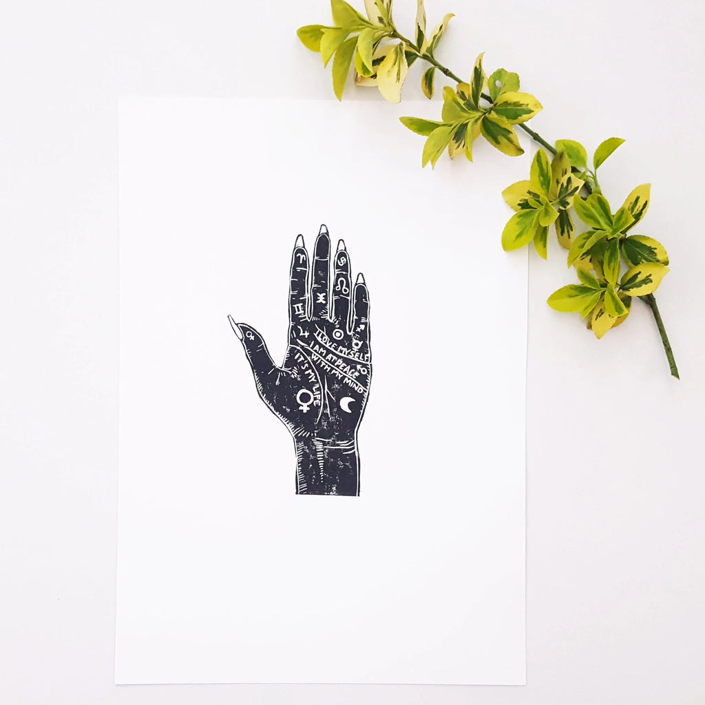 Decorative black hand-shaped object with white patterns next to a branch of green leaves on a white background