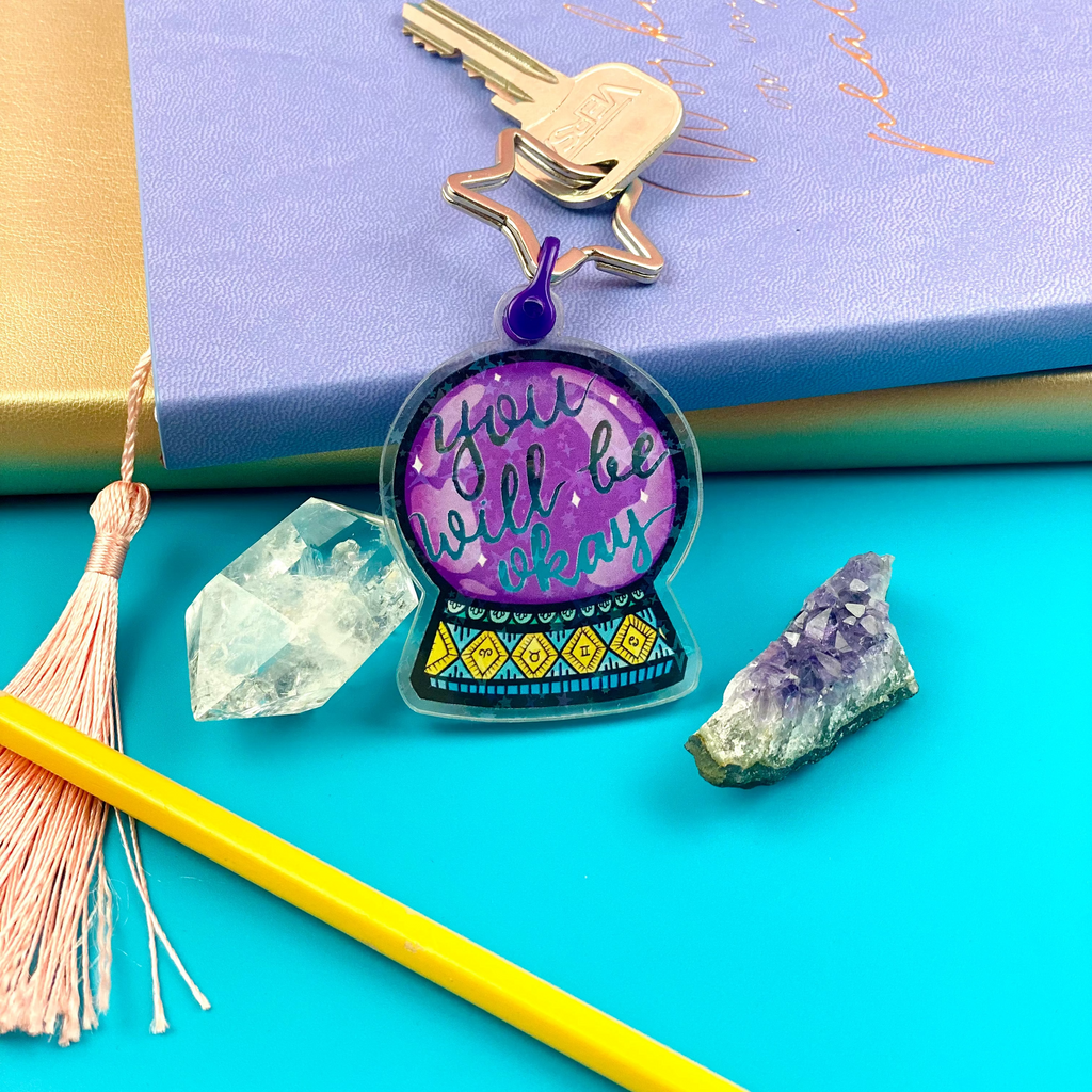 Keychain with 'You will be okay' message on a blue background with crystals and a pencil.